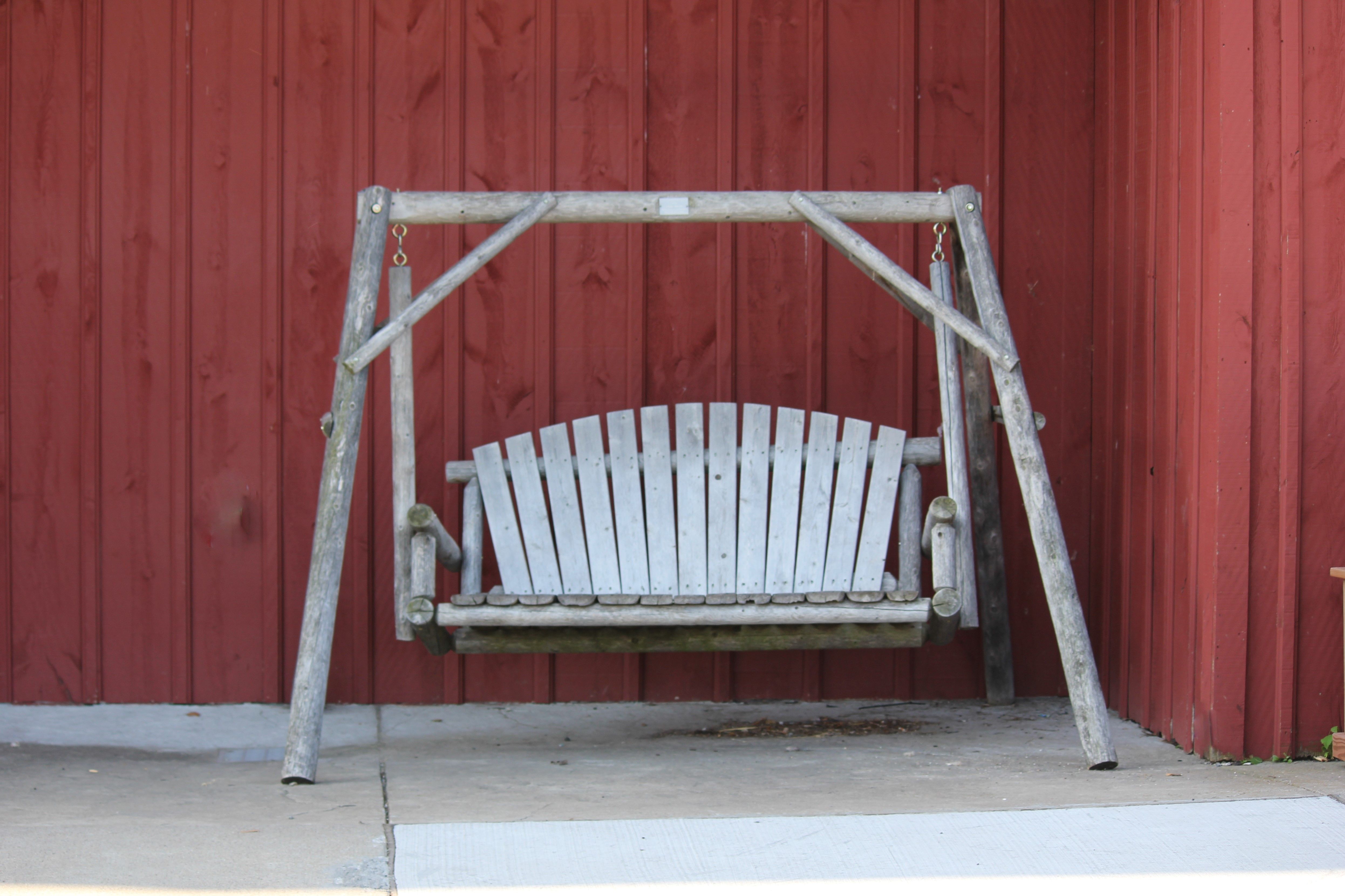 Rustic wooden swing bench against a deep red barn wall