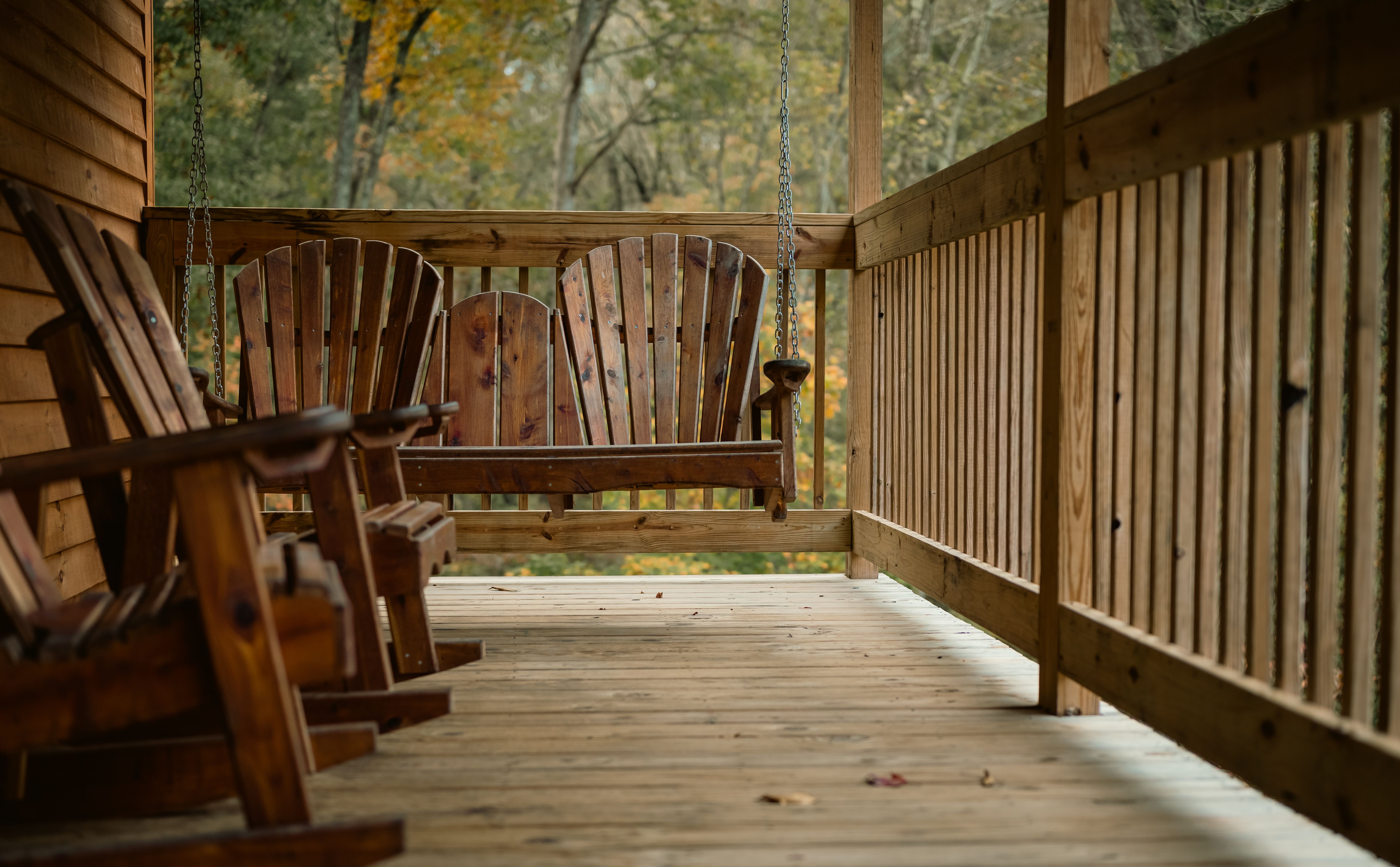 Serene wooden porch with a rustic hanging swing amid autumn foliage